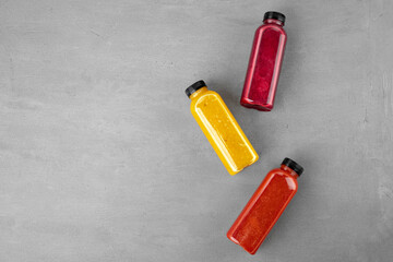 Three plastic bottles with freshly squeezed juice on gray background