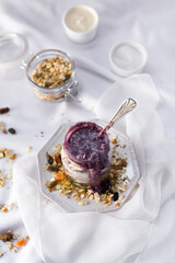 Frasco de vidrio con granola, yogur y mermelada de arándanos sobre fondo blanco