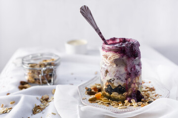 Frasco de vidrio con granola, yogur y mermelada de arándanos sobre fondo blanco