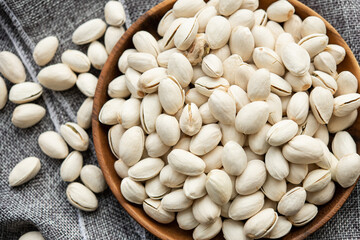 Wooden bowl with nut pistachios.  on a wooden background, near a bag from burlap. Healthy food and snack, organic vegetarian food. (selective focus; close-up shot)
