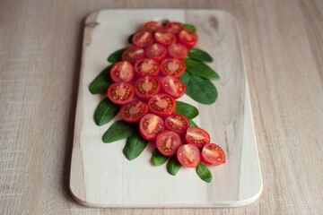 Small red cut cherry tomatoes lie curly on a wooden board on a wooden background and green spinach leaves