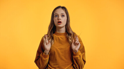 teenager in sweater with crossed fingers and open mouth isolated on yellow