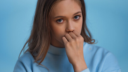 worried teenage girl in sweatshirt looking at camera isolated on blue