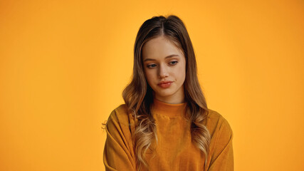 pensive teenage girl in sweater looking down isolated on yellow