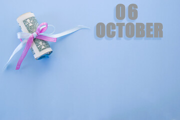 calendar date on blue background with rolled up dollar bills pinned by blue and pink ribbon with copy space.  October 6 is the sixth day of the month