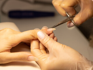 Close up of manicurist hands clipping client nails. Young woman getting manicure treatment. Clipping nails, hand care and nail care at beauty salon. Selective focus.