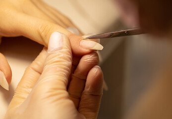 Close up of manicurist hands clipping client nails. Young woman getting manicure treatment. Clipping nails, hand care and nail care at beauty salon. Selective focus.