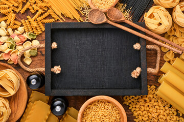 Variety of traditional italian pasta: colorful spaghetti, tagliatelle, farfalle, penne, ptititm, noodle, fusilli, cannelloni on an old wooden background. Top view with copy space.