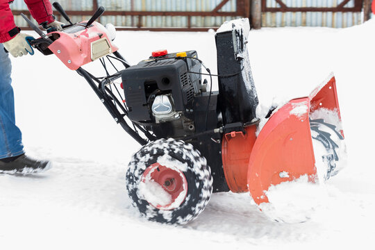 A man-driven snowblower moving along the snow along the fence. Selective focus.