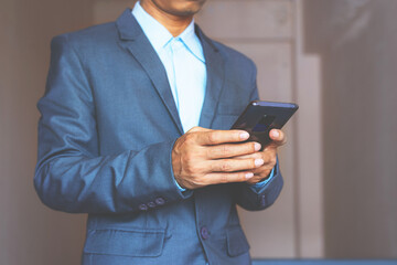 close up of business man hand using smart phone touch on screen and typing for some searching internet information technology data against gray wall background.