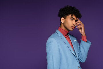 Fototapeta na wymiar pierced african american man in blue blazer looking at camera while posing on purple