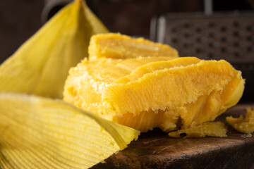 Pamonha, Brazilian corn food, called pamonha. On a rustic table with knife and old corn grater, low key portrait, dark abstract background, selective focus.