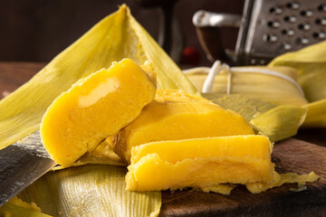 Pamonha, Brazilian corn food, called pamonha. On a rustic table with knife and old corn grater, low key portrait, dark abstract background, selective focus.