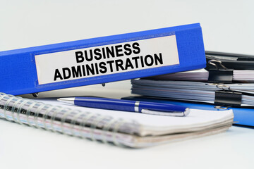 On the table are a notebook, a pen, documents and a folder with the inscription - BUSINESS ADMINISTRATION
