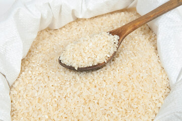 wooden spoon with rice lying on a pile of rice in a bag close up on a white background isolated