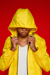 stylish african american man in yellow rain jacket with hood isolated on red