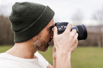 Profile of a man with a cap taking a photo outdoors