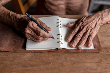 old man writing with a pencil in a notebook,Handwriting on the wood desk