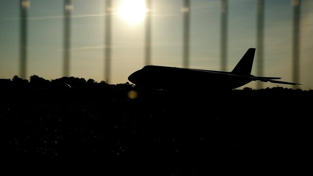 Dark silhouette of an airplane at sunset approach in the airport a beautiful sky, aircraft. In foreground is barrier grid