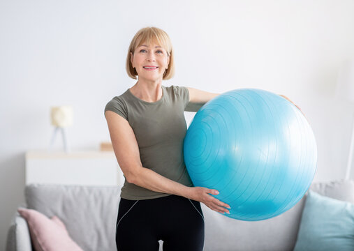 Portrait of joyful senior woman holding fitness ball and smiling at camera, indoors