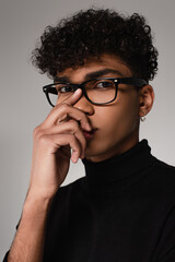 curly african american man in turtleneck sweater adjusting glasses isolated on grey