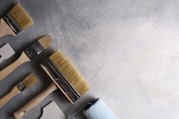 Spatulas for application of putty and brushes and rollers for painting on a gray concrete background.Top view