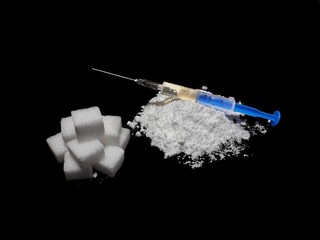 Injection syringe on cocaine drug powder pile and lump sugar cubes on black background, sugar is more addictive than cocaine, isolated cubes of white sugar and cocaine on black background