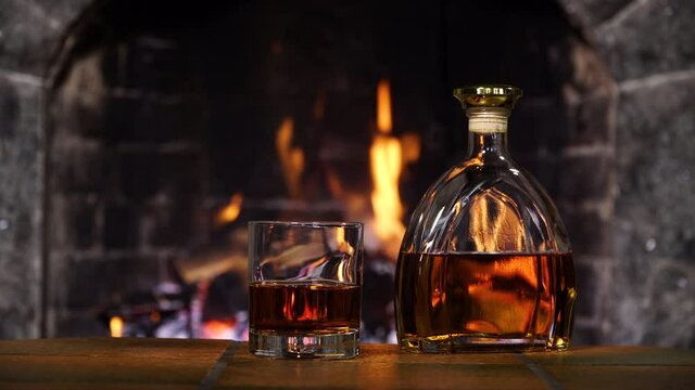 Bottle and glass with whiskey or cognac. Burning Fire In The Fireplace. Warmth and home comfort. 4K