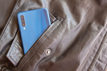 Modern 3d camera smart phone in leather jacket pocket. Top view of blue gadget, horizontal...