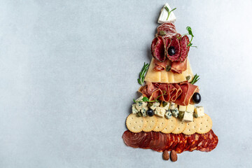 Antipasto or Italian appetizers with ham, prosciutto, salami, cheese, crackers and capers laid out in the shape of a Christmas tree. top view