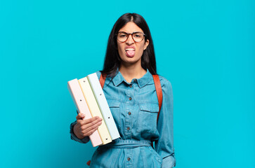young hispanic student woman feeling disgusted and irritated, sticking tongue out, disliking...