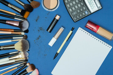 Make up the essentials. A set of professional makeup brushes and cosmetics on a blue background. Next to it is a notebook with a pencil. Perfect for a beauty blog. Flatly, horizontal.