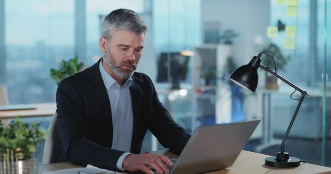 Portrait of handsome successful adult employe using portable laptop computer smiling inside office. Business people at work.