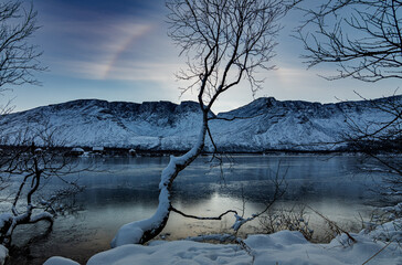 Solar halo in the mountains near a lake covered with ice on a winter evening