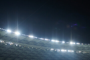 Stadium lit floodlighting into the darkness of the evening. Bokeh effect. - 417653533