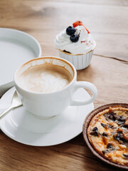 Morning breakfast in a cafe on a brown background. aromatic coffee in a white mug with a tartlet with mushrooms and a french dessert with blueberries and strawberries