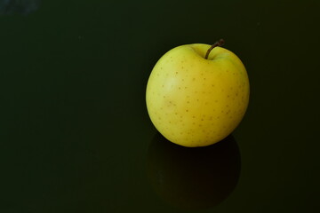 a yellow apple on a black glass surface