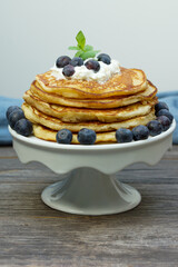 stack of American pancakes with cream and blueberries on a white cake plate