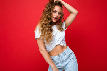 Young beautiful curly blonde woman with sexy expression, cheerful and happy face wearing casual white t-shirt isolated over red background with copy space