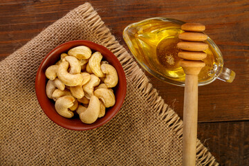 Cashew nuts in a bowl on sacking next to honey with a spoon on a wooden table.