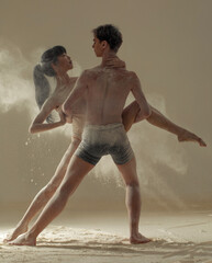 Two ballet dancers perform dance against background of white flour cloud in air.