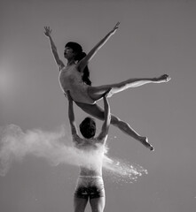 Two ballet dancers perform dance against background of white flour cloud in air.