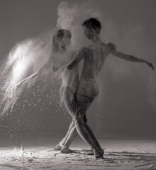 Obraz na płótnie Canvas Two ballet dancers perform dance against background of white flour cloud in air.