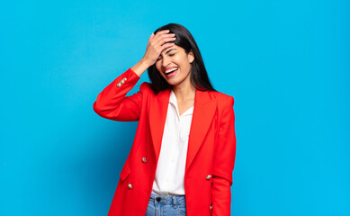 young hispanic businesswoman laughing and slapping forehead like saying d’oh! I forgot or that...