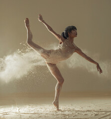 Ballerina performs arabesque pose against background of white flour cloud in air.