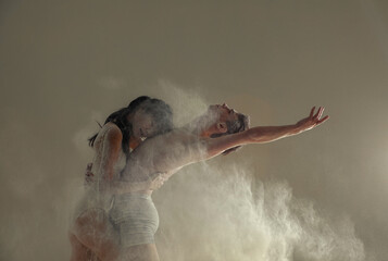 Two ballet dancers dance against white flour cloud in air.