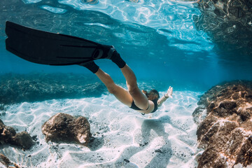 Freediving underwater in blue ocean. Sporty woman free diver swim with fins and corals.