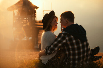 Couple in love sitting closely on riverside during sunset
