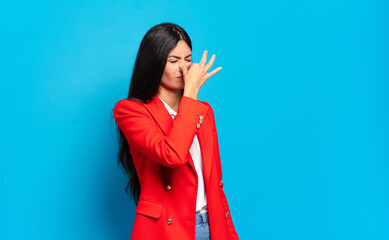 young hispanic businesswoman feeling disgusted, holding nose to avoid smelling a foul and...