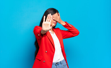 young hispanic businesswoman covering face with hand and putting other hand up front to stop...